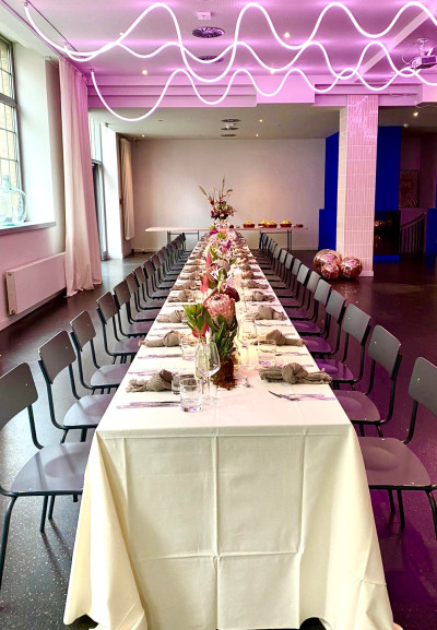 Long banquet table with a pink lighting installation on the ceiling at event venue Frankfurt GOOSE Eventspace